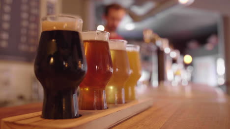 Glasses-of-artisanal-beer-on-a-bar-counter-with-barman-pouring-draft-beer